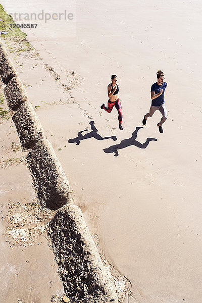 Junger Mann und Frau laufen am Strand entlang  erhöhte Ansicht