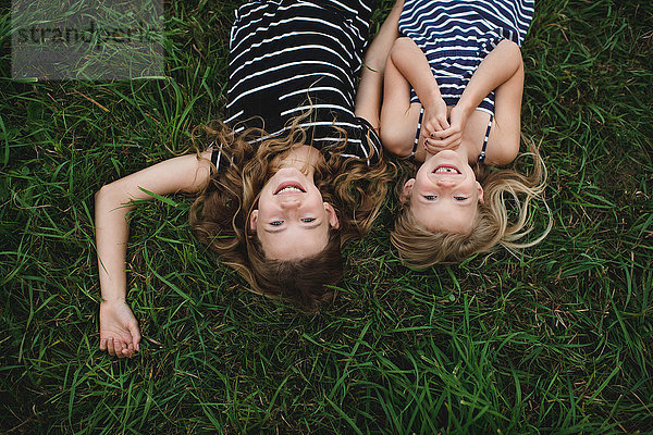 Auf dem Kopf stehendes Porträt eines Mädchens und ihrer Schwester im Gras liegend
