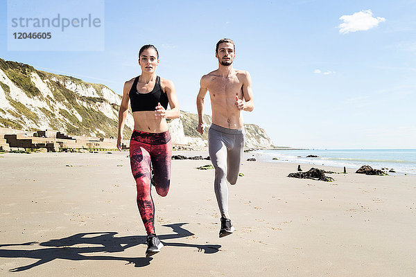 Junger Mann und Frau laufen am Strand entlang  Frontansicht
