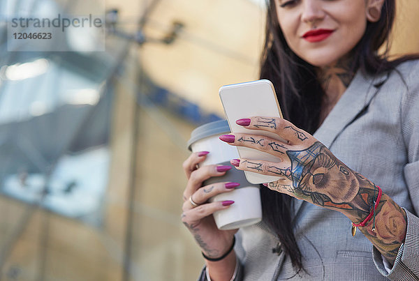 Geschäftsfrau im Freien  Kaffeetasse haltend  Smartphone benutzen  Tätowierungen an den Händen  Mittelteil