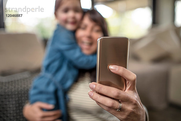 Leichte Konzentration einer reifen Frau  die mit ihrer Tochter im Wohnzimmer ein Smartphone-Selfie mitnimmt