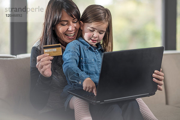Mädchen und Mutter auf dem Sofa mit Laptop und Kreditkarte beim Online-Shopping