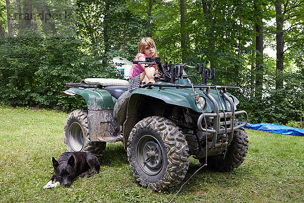 Porträt eines Mädchens auf einem Quad-Bike sitzend  Hund entspannt daneben