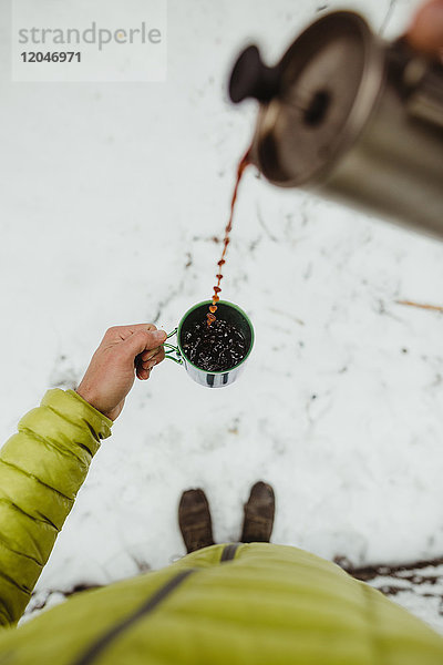 Persönliche perspektivische Ansicht eines männlichen Wanderers  der im Schnee Kaffee aus der Flasche gießt