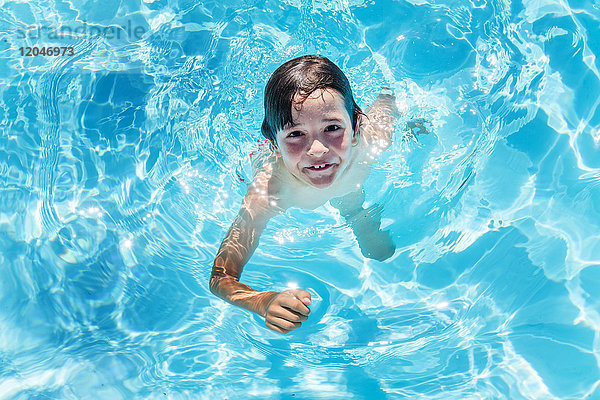 Portrait eines Jungen  der im sonnenbeschienenen Swimmingpool im Freien Wasser tritt