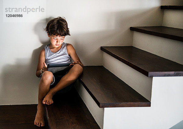 Junge sitzt auf einer Treppe und starrt auf ein digitales Tablett