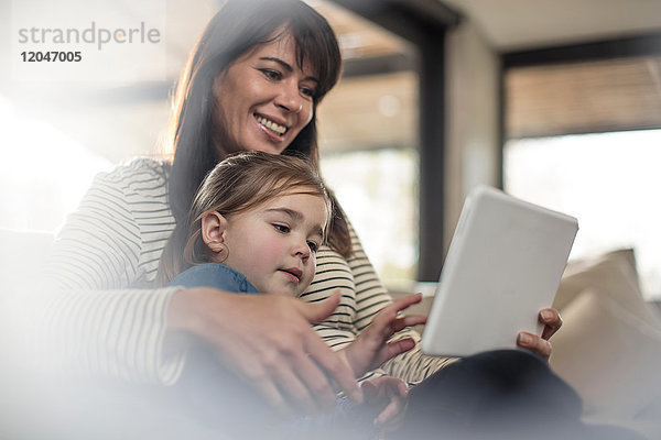 Frau mit Tochter auf Sofa schaut auf digitales Tablet