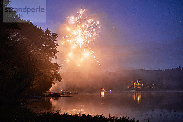 Feuerwerkskörper explodieren in der Abenddämmerung über dem See