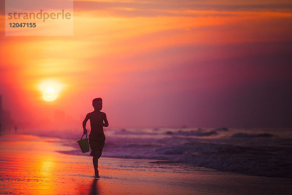 Silhouette eines Jungen  der bei Sonnenuntergang am Strand läuft  North Myrtle Beach  South Carolina  Vereinigte Staaten