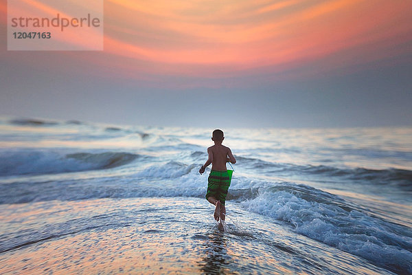 Junge läuft bei Sonnenuntergang ins Meer  North Myrtle Beach  South Carolina  Vereinigte Staaten