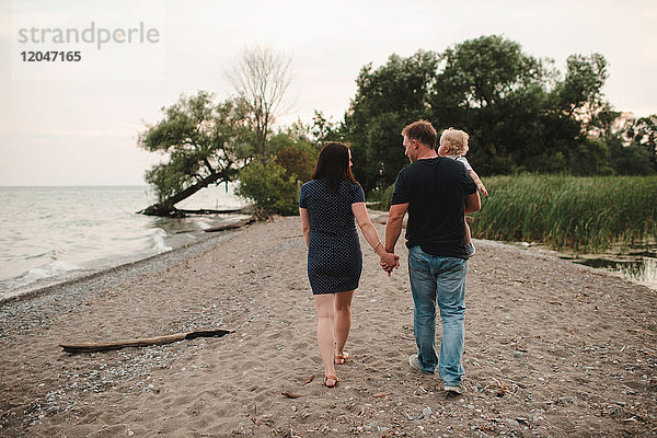 Rückansicht eines Paares  das mit einem männlichen Kleinkind am Strand spazieren geht  Ontariosee  Kanada