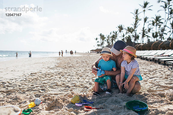 Vater sitzt mit kleinem Sohn und Tochter am Strand