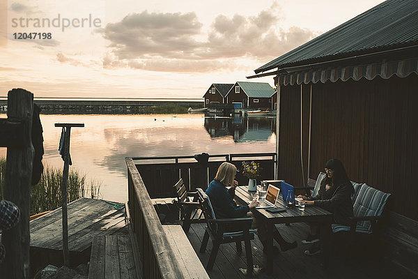 Freunde mit Laptop am Tisch in der Ferienvilla am See gegen den Himmel