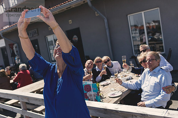 Seniorenfrau mit Freunden  die mit dem Handy auf der Terrasse des Restaurants telefonieren.