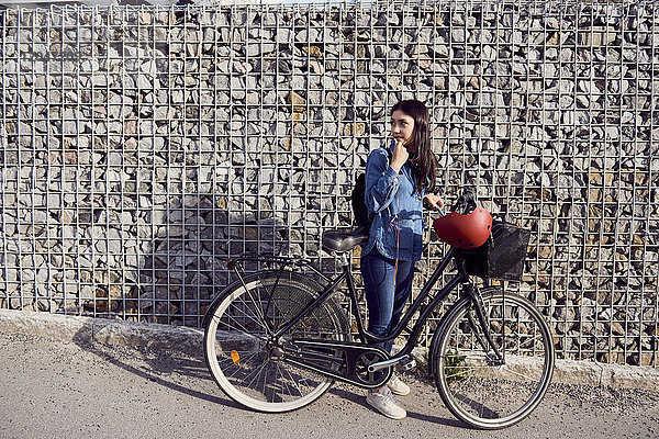 Volle Länge der Frau  die im Stehen mit dem Fahrrad gegen die Steinmauer schaut.