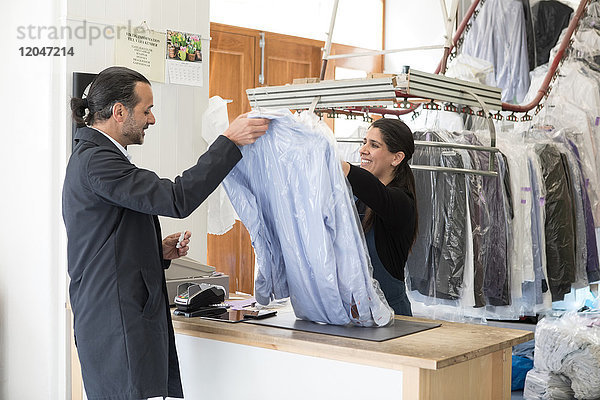 Lächelnde reife Besitzerin  die dem männlichen Kunden an der Kasse T-Shirts schenkt.