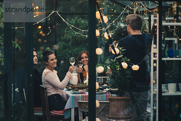 Mann  der junge Freunde fotografiert  die während der Dinnerparty mit Weingläsern anstoßen.