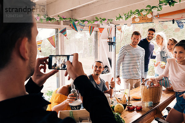 Mann fotografiert Freunde auf dem Smartphone in der Hütte