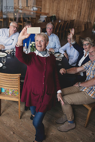 Glückliche Seniorenfrau  die sich mit Freunden über Handy im Restaurant vergnügt.