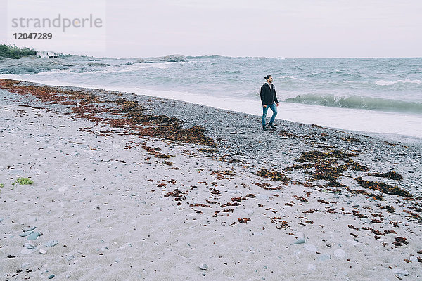 Volle Länge des jungen Mannes  der über das Meer am Strand läuft.