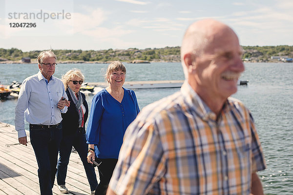Glückliche Seniorinnen und Senioren  die im Urlaub am Pier spazieren gehen.