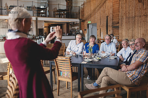 Seniorin fotografiert glückliche Freunde am Tisch im Restaurant