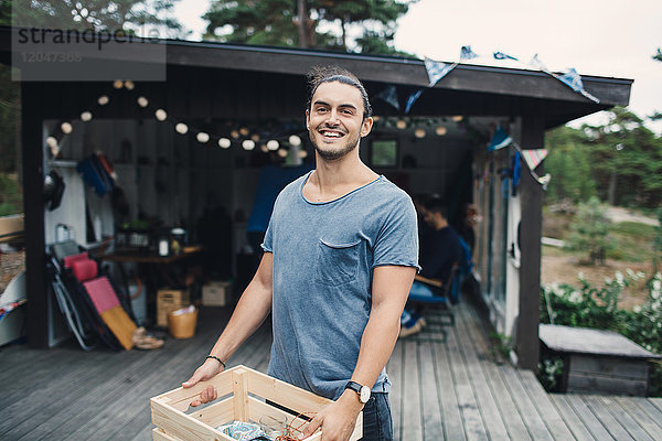 Porträt eines glücklichen jungen Mannes mit Holzkiste auf der Veranda im Hinterhof