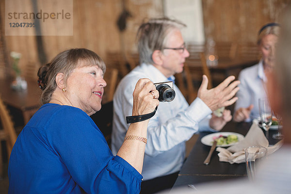 Seniorin fotografiert mit der Kamera  während sie mit Freunden im Restaurant sitzt