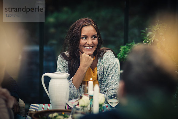 Lächelnde junge Frau sitzt am Esstisch während der Party im Hinterhof