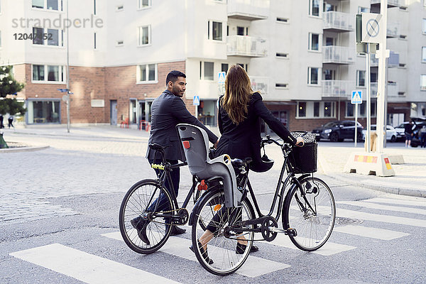 Rückansicht von Geschäftspartnern mit Fahrrädern über die Straße in der Stadt
