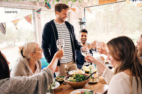Fröhlicher Mann toastet mit Freunden bei der Mittagsparty auf Weinglas
