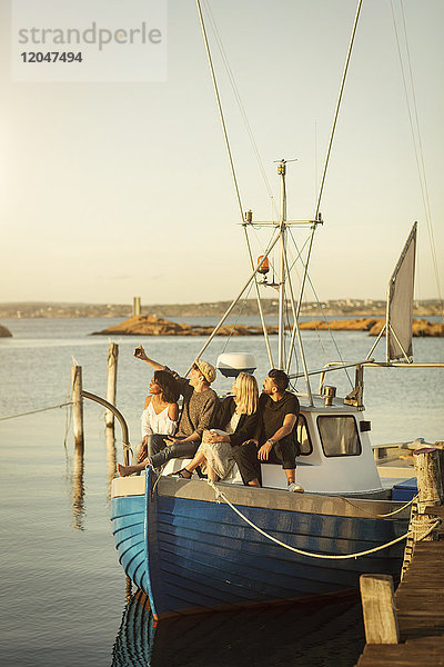 Junger Mann nimmt Selfie mit Freunden mit  während er auf einem Boot sitzt  das am Hafen festgemacht ist.