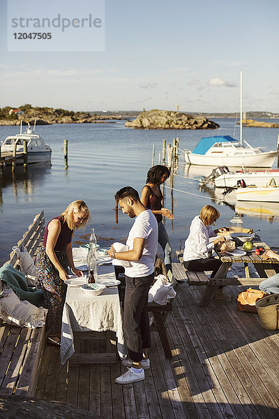 Junge multiethnische Freunde bereiten das Mittagessen im Hafen gegen den Himmel an einem sonnigen Tag vor.