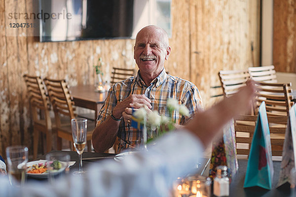 Lächelnder älterer Mann  der einen Freund ansieht  während er am Tisch im Restaurant sitzt.