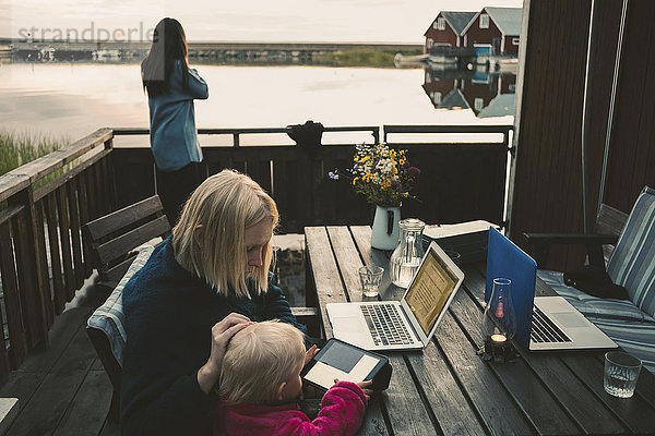 Frau unterrichtet Tochter bei der Benutzung des digitalen Tabletts  während ein Freund auf dem Handy spricht.