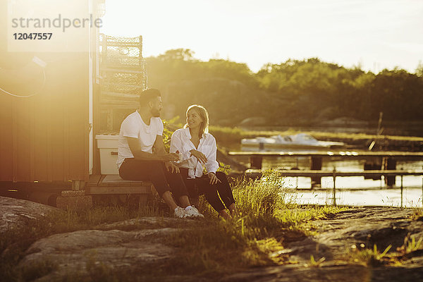 Volle Länge des glücklichen jungen Paares beim Sitzen in der Blockhütte an einem sonnigen Tag.
