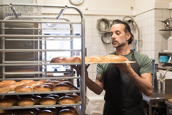 Zuversichtlicher  reifer Mann mit Backblech und frisch gebackenem Brot in der Bäckereiküche.
