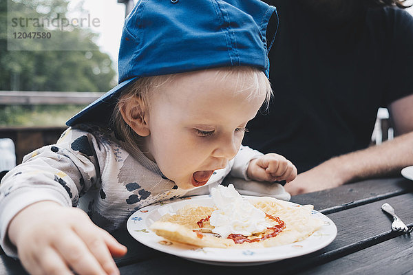 Mädchen mit geöffnetem Mund beim Essen beim Sitzen beim Vater am Tisch