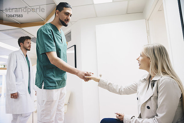 Seitenansicht der Patientin beim Händeschütteln mit dem jungen Krankenpfleger im Krankenhaus