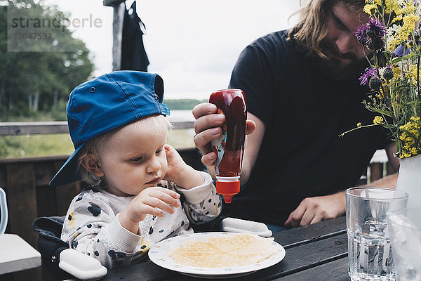 Mädchen sieht Vater an  wie er Honig auf Waffeln am Tisch drückt