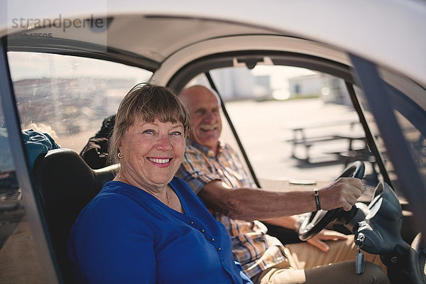 Porträt einer lächelnden älteren Frau und eines Mannes  die an einem sonnigen Tag eine Autofahrt genießen.