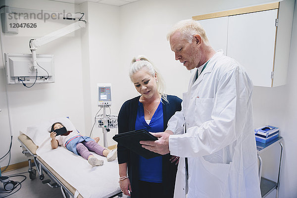 Reife Ärztin zeigt der Frau  die im Krankenhaus am Bett steht  eine digitale Tablette.