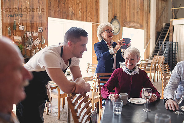 Junger Kellner  der sich auf den Stuhl lehnt  während sich ältere Freunde im Restaurant treffen.