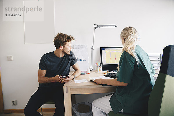 Männlicher Patient schaut  während die Krankenschwester den Computer im Krankenhaus benutzt.