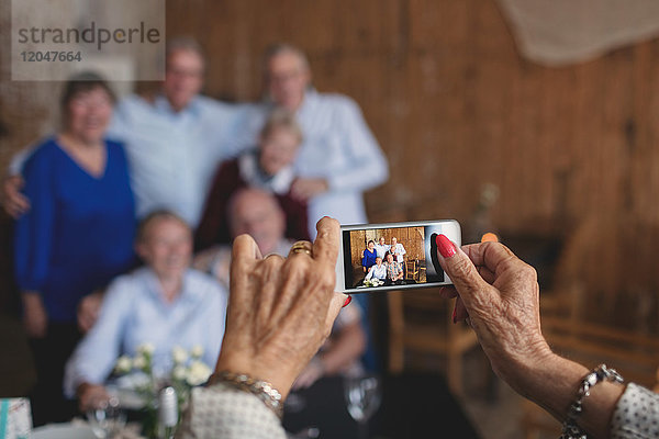 Abgeschnittenes Bild einer älteren Frau  die Freunde mit dem Smartphone im Restaurant fotografiert.