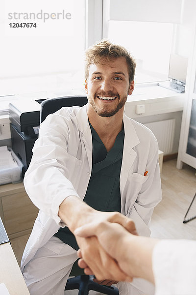 Porträt eines lächelnden jungen Arztes  der der Krankenschwester im Krankenhaus die Hand schüttelt