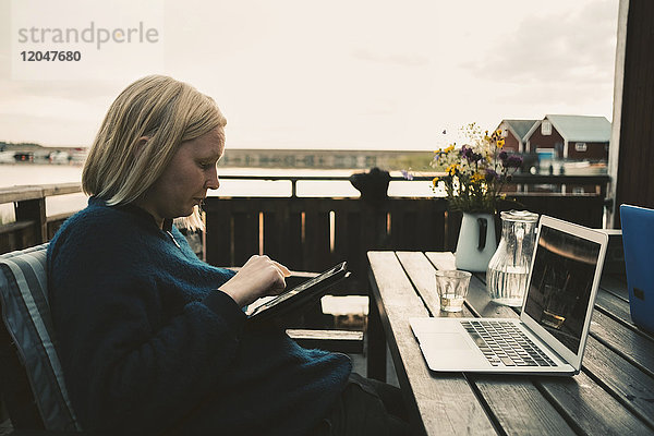 Frau mit digitalem Tablett und Laptop auf Holztisch in der Ferienvilla