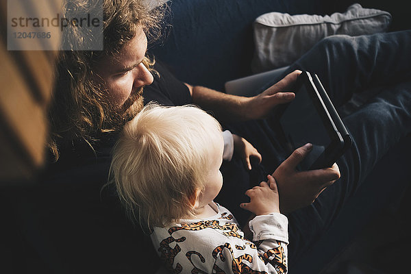 Vater zeigt dem Mädchen auf dem Sofa zu Hause ein digitales Tablett.