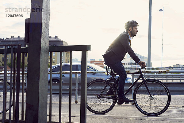 Seitenansicht des Geschäftsmannes beim Radfahren auf der Straße gegen den Himmel