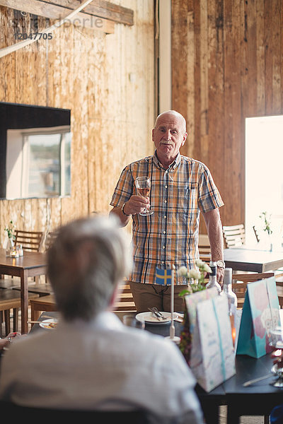 Senior Mann hält Weinglas  während er mit einem Freund im Restaurant spricht.